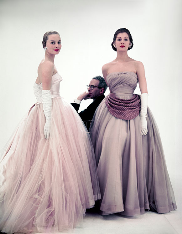 British fashion designer Norman Hartnell, best known for his work for the ladies of the Royal Family, photographed for Vogue magazine, 1953. On the far right, model Fiona Campbell-Walter.
