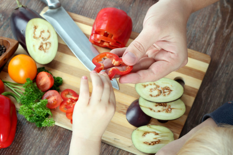 food, family, cooking and people concept - Man chopping paprika on cutting board with knife in kitchen with daughter